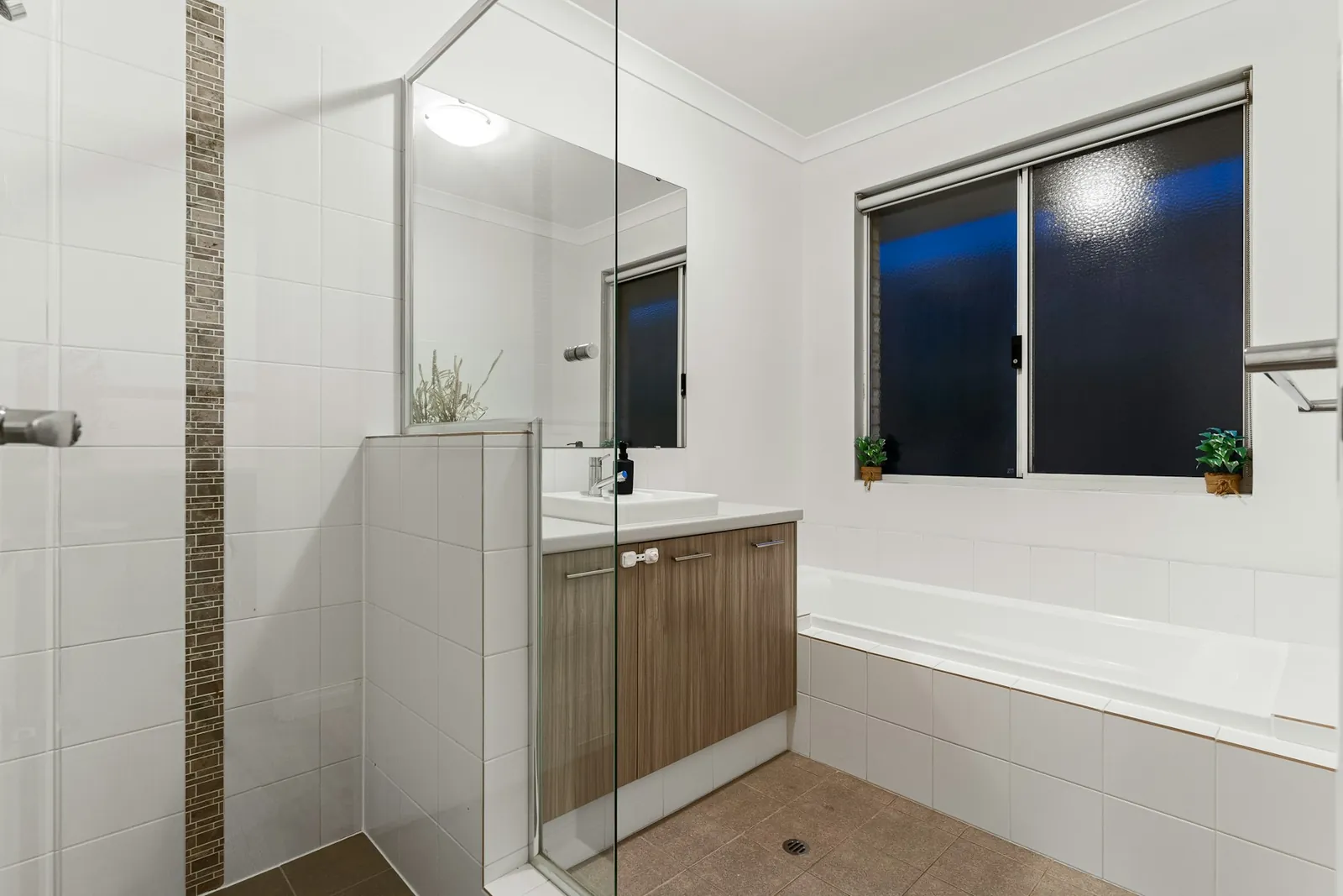 Baño con ducha acristalada, lavabo y bañera, junto a una ventana