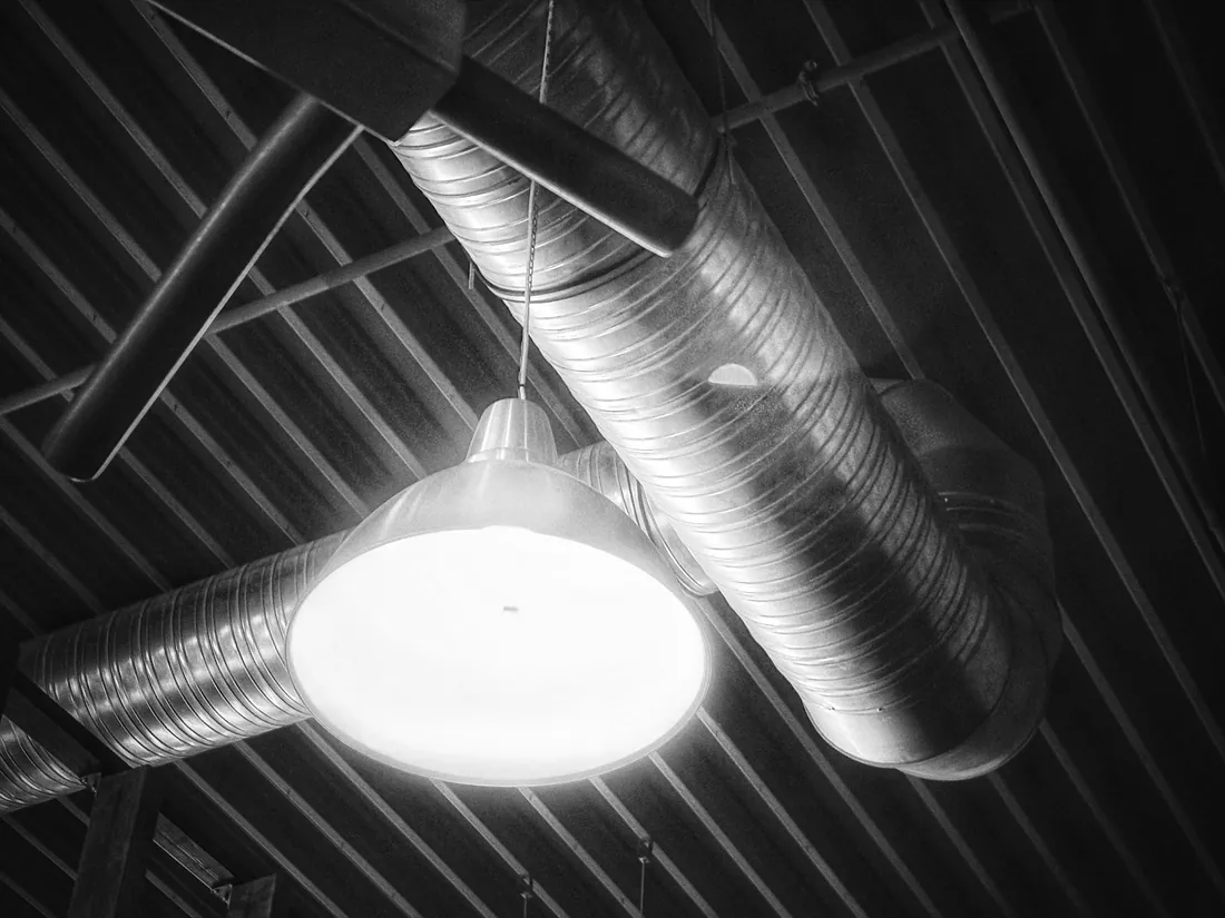 Conductos metálicos vistos y una luminaria colgante bajo un techo industrial