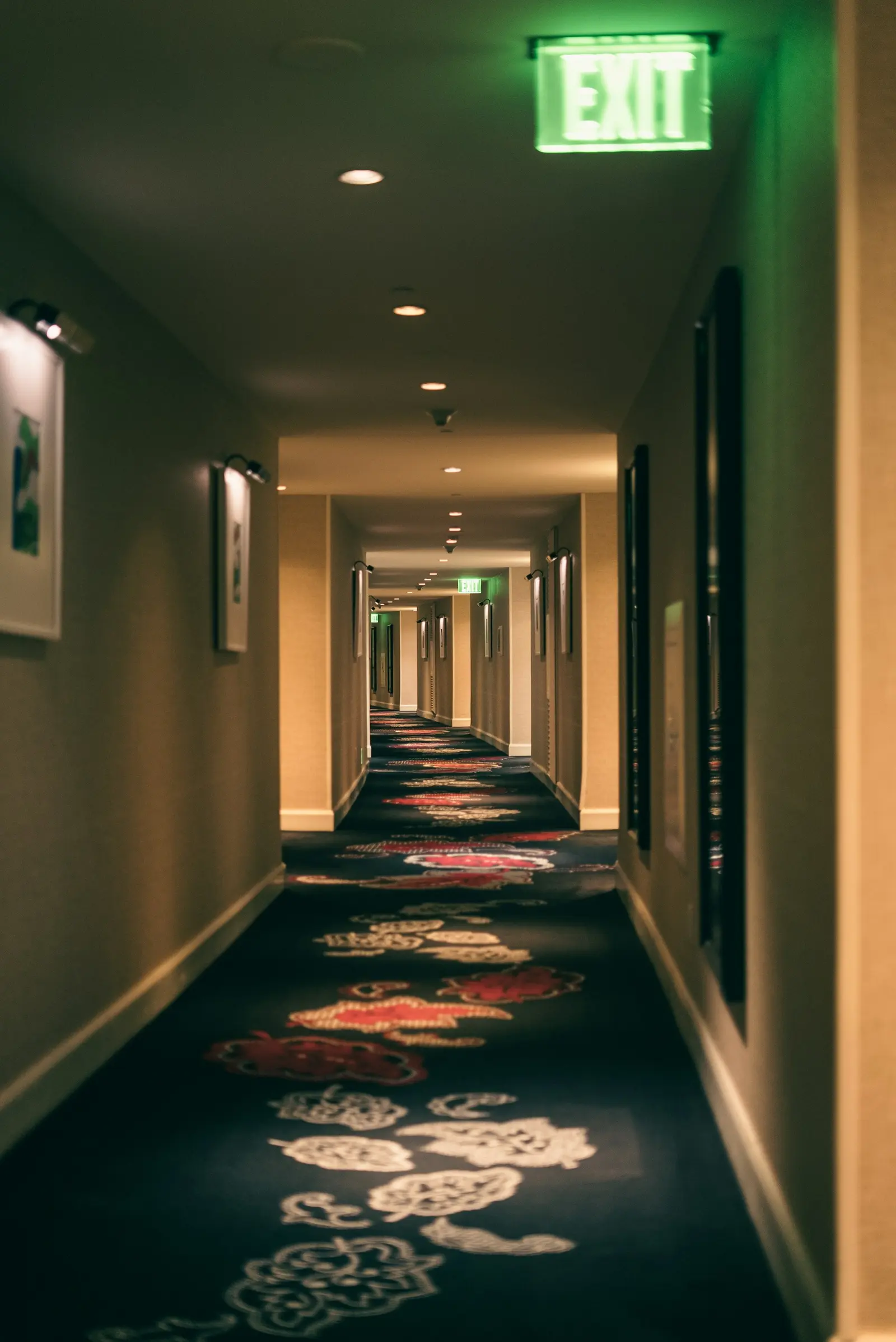 Pasillo de hotel con moqueta estampada, puertas laterales y señal de salida