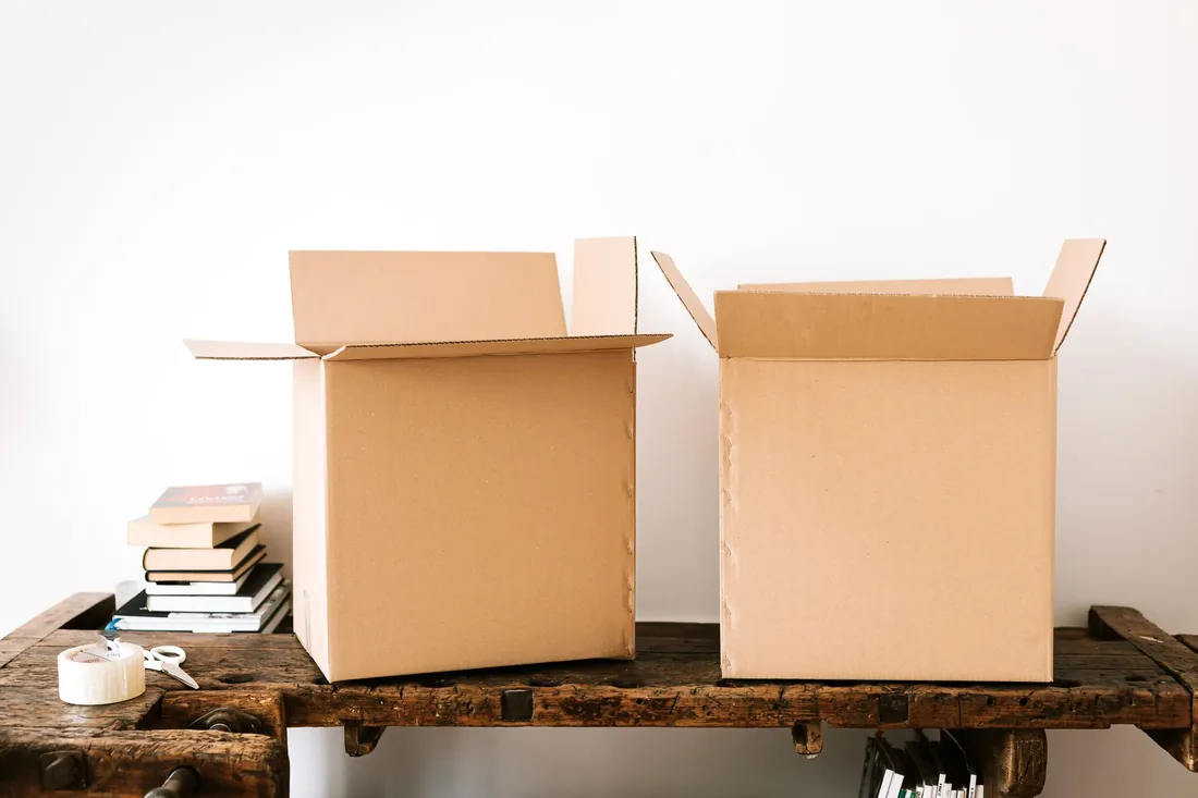 Cajas de cartón abiertas, libros y cinta de embalaje sobre una mesa de madera