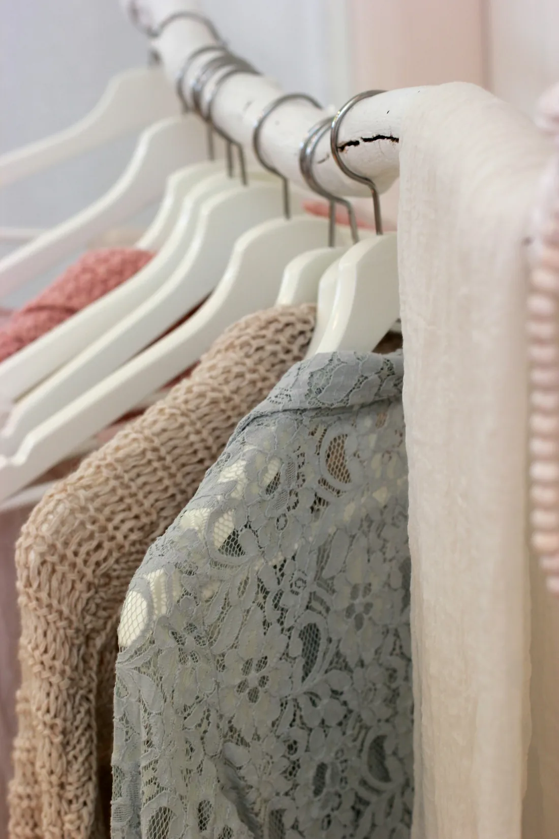 Prendas de varios colores colgadas en perchas sobre una barra blanca
