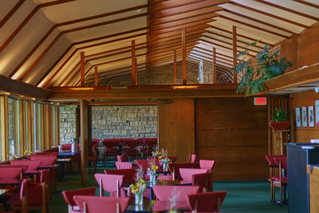 Comedor con mesas, sillas rojas y estructura de madera en el techo