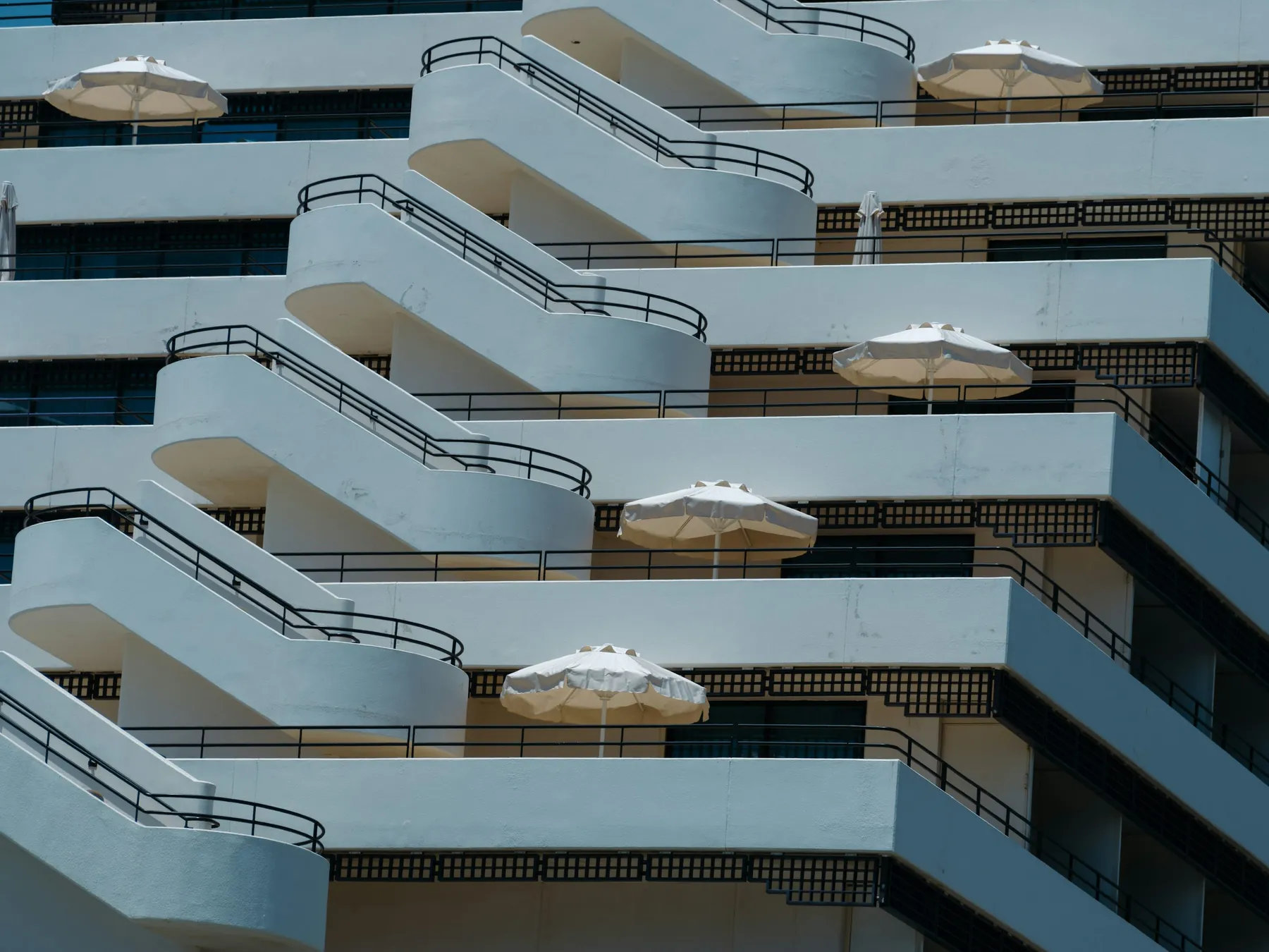 Fachada de hotel com varandas brancas, guardas e zonas de sombra