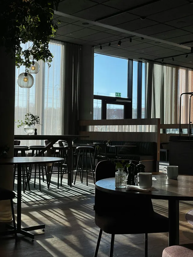 Restaurante de hotel con ventanales, mesas de madera e iluminación suspendida