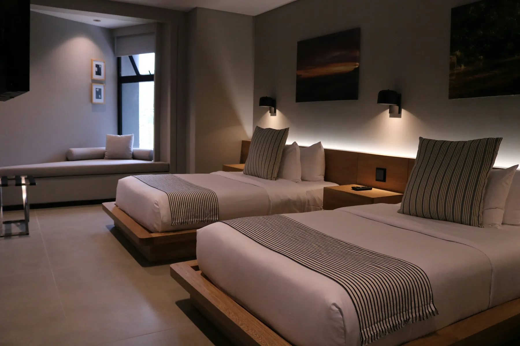 Habitación de hotel con dos camas, bases de madera e iluminación integrada